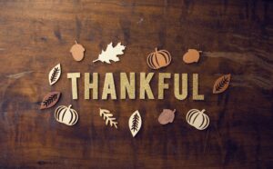 The word THANKFUL in gold letters laid on a wooden table, surrounded by crafty cutouts of leaves and pumpkins