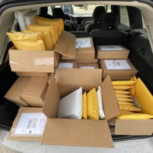 Dozens of shipping boxes and mailing envelopes, stacked in the back of a large hatchback car.