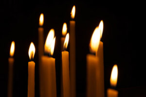 a group of white taper candles, lit, against a dark background