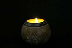 A spherical candle, brown with white etched patterns on it. The candle's light is the only light in the image,